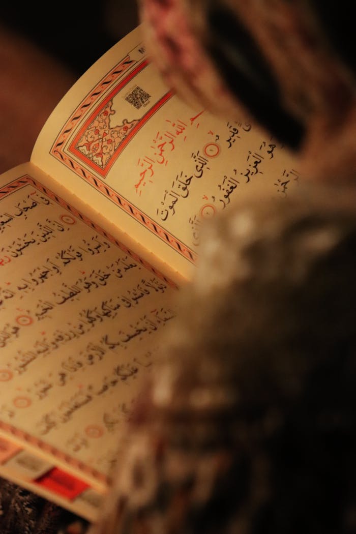 The Art of Drawing Readers In: Your attractive post title goes here A close-up of a person reading the Quran with a focus on Arabic script and warm lighting.